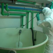 Dos personas con trajes azules de sala limpia se desinfectan las manos en un laboratorio.